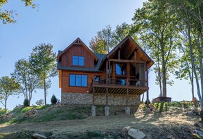 Ein zweigeschossiges Holzhaus mit Steinfundament, einem Balkon und einer Steismauer.