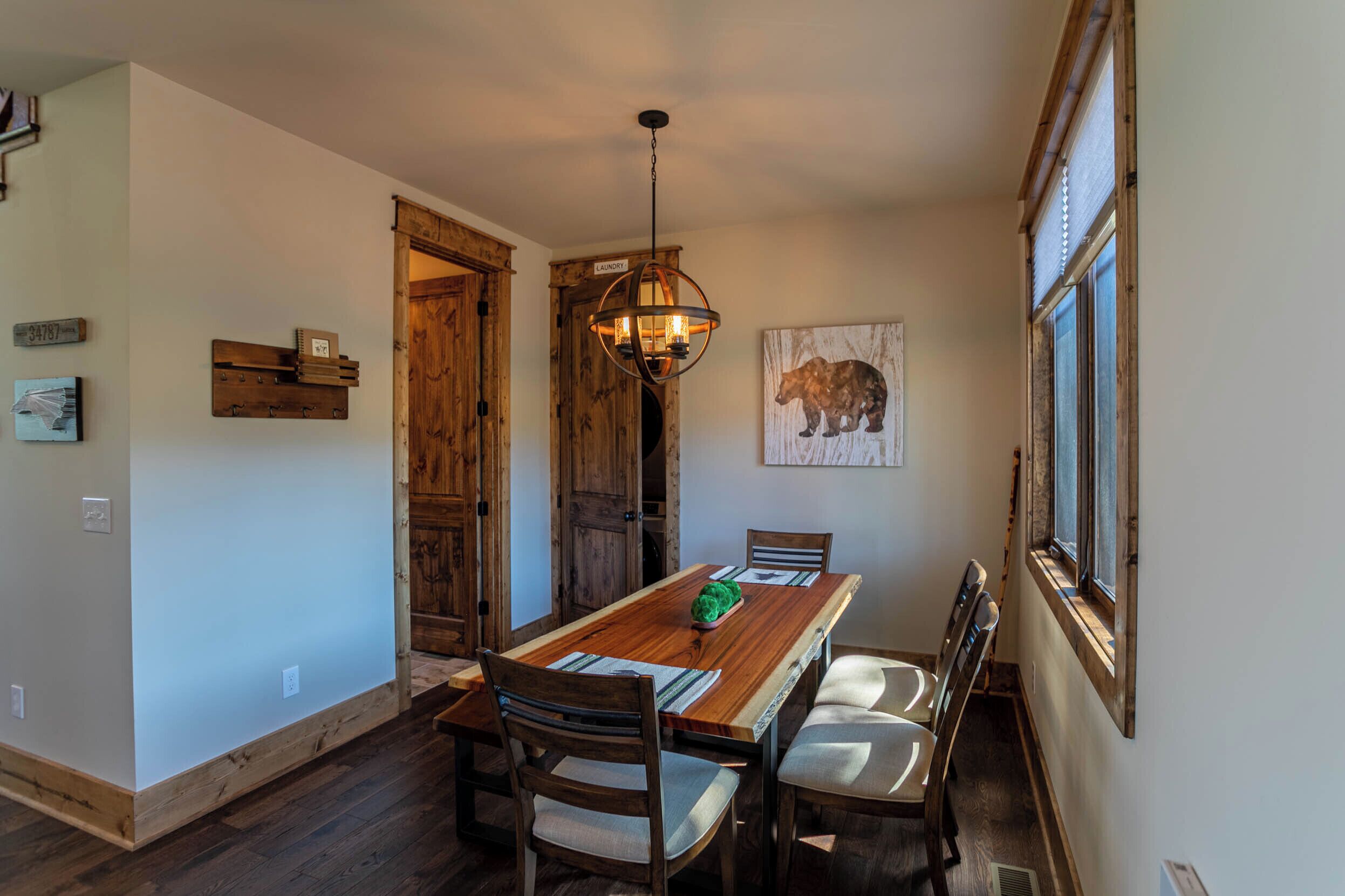 Un'area pranzo con un tavolo in legno, sedie, un lampadario a sospensione, una porta in legno e un quadro di un orso al muro.