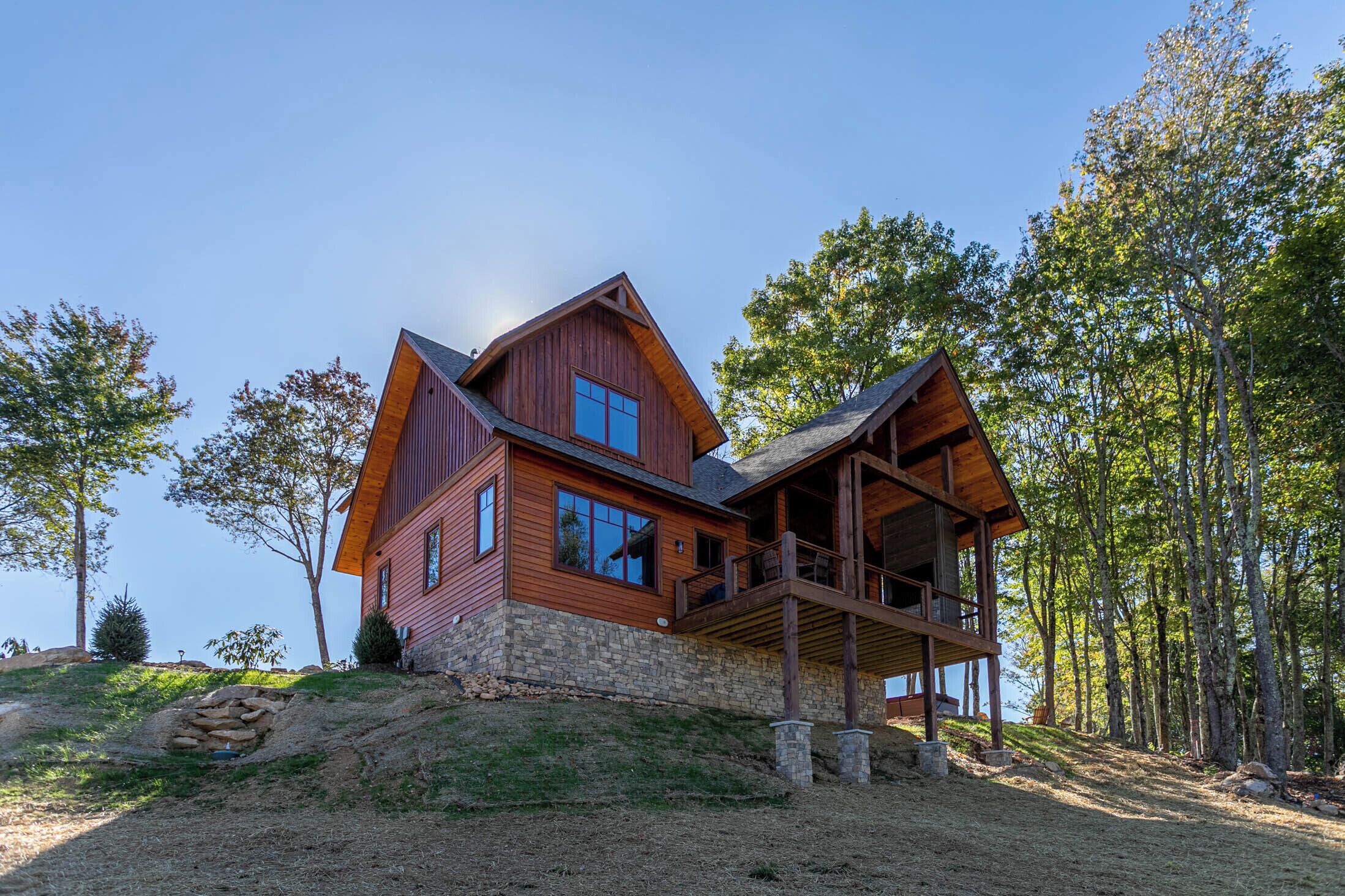 A two-story wooden cabin with a stone foundation, large windows, and a balcony.