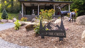 A lodge with a stone facade, a porch, and a deer statue. - Up the Creek (Linville)