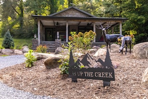 A lodge with a stone facade, a porch, and a deer statue. - Up the Creek (Linville)