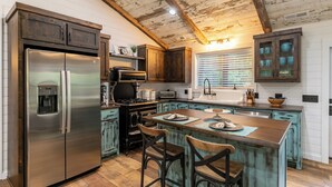 A kitchen with a stainless steel refrigerator, wooden cabinets, a central island with bar stools, and a rustic ceiling. - Up the Creek (Linville)