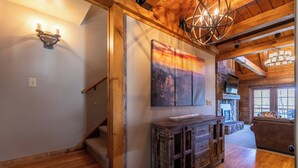Una escalera de madera conduce a una zona superior con una chimenea, un gabinete de madera rústica y un cuadro grande en la pared.