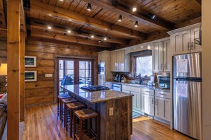 Una cocina con vigas de madera, una isla central con taburetes, electrodomésticos de acero inoxidable y armarios blancos.