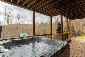 Jacuzzi en una terraza de madera con vista a un área boscosa.