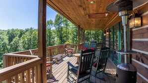 Una terraza de madera con mobiliario exterior, un cubo de basura y vistas al bosque.