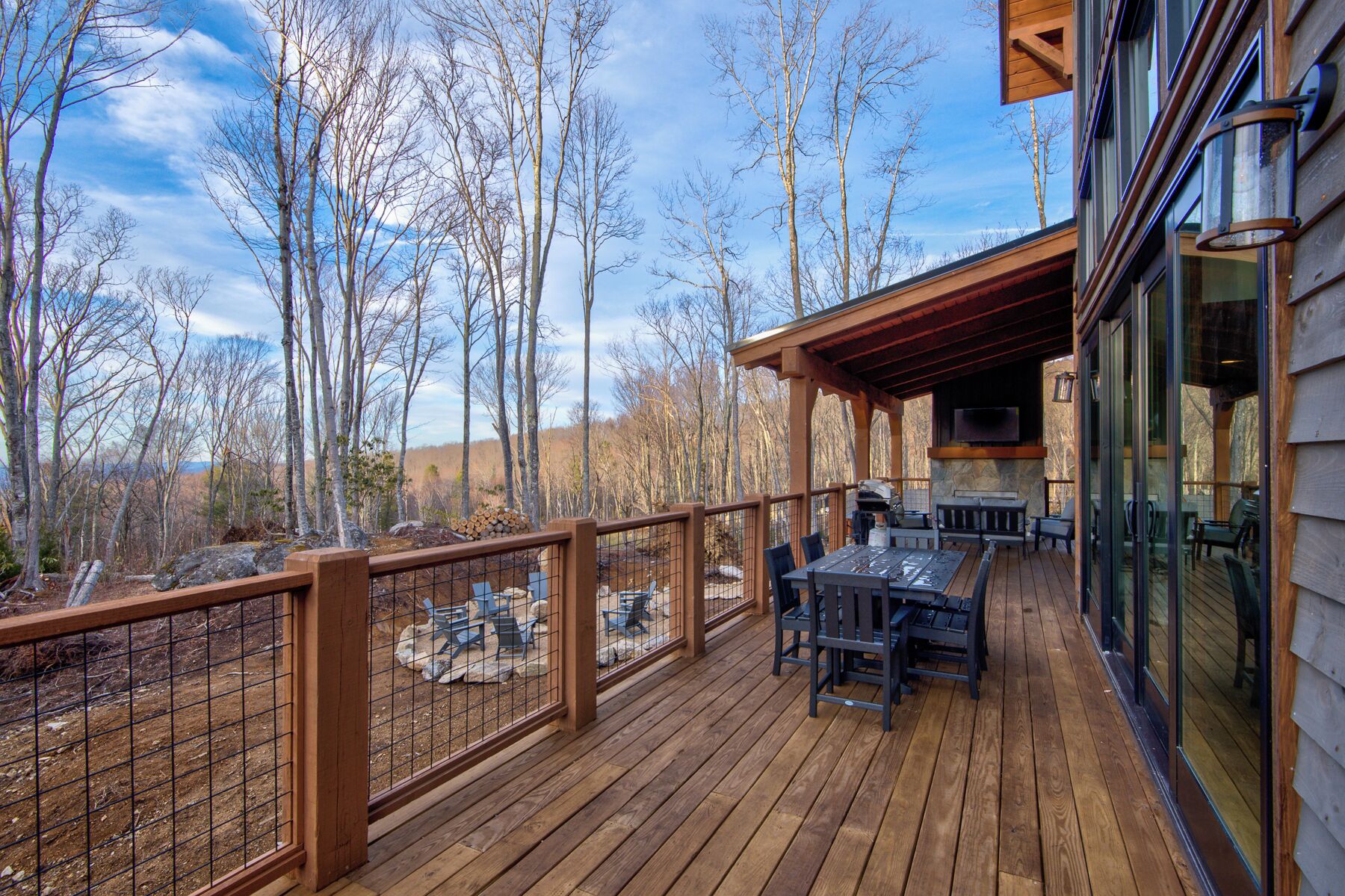 Una terraza de madera con mobiliario exterior, una chimenea de piedra y un televisor montado en la pared.