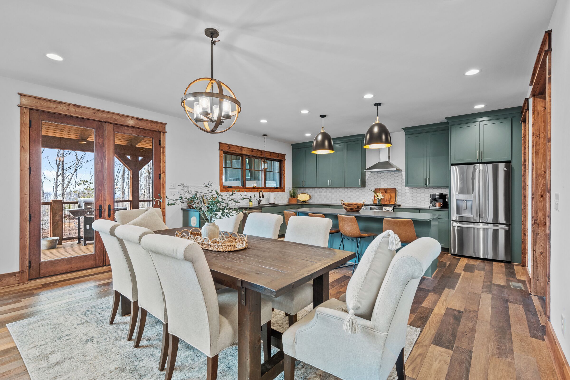 A modern kitchen with a dining area, wooden flooring, and a large window overlooking a deck.