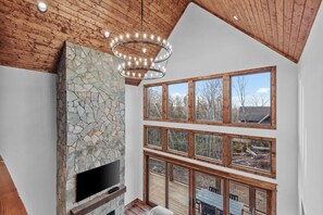 Ein modernes Interieur mit Kamin aus Stein, großen Fenstern und einer Holzbalkendecke.