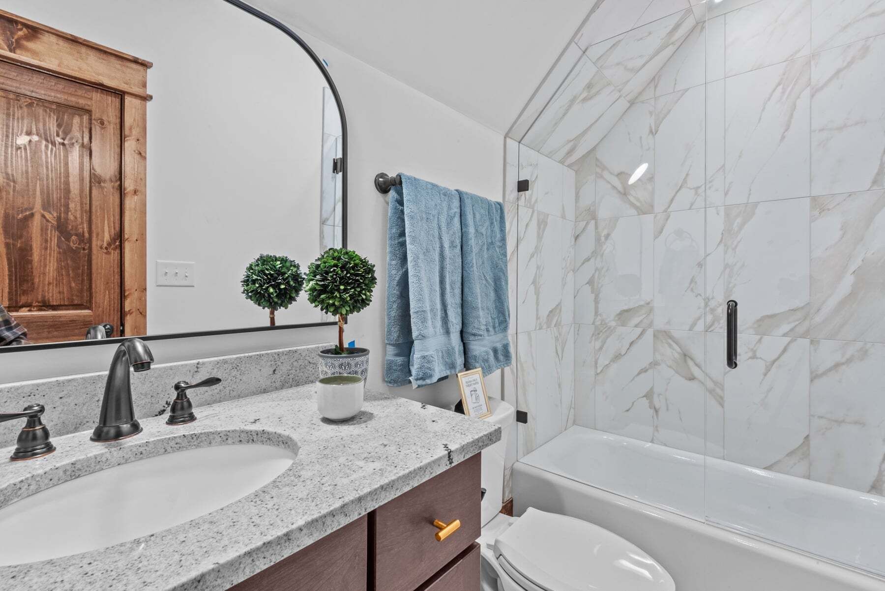 Une salle de bain avec un lavabo, un miroir, une serviette, des toilettes et un mur en marbre.