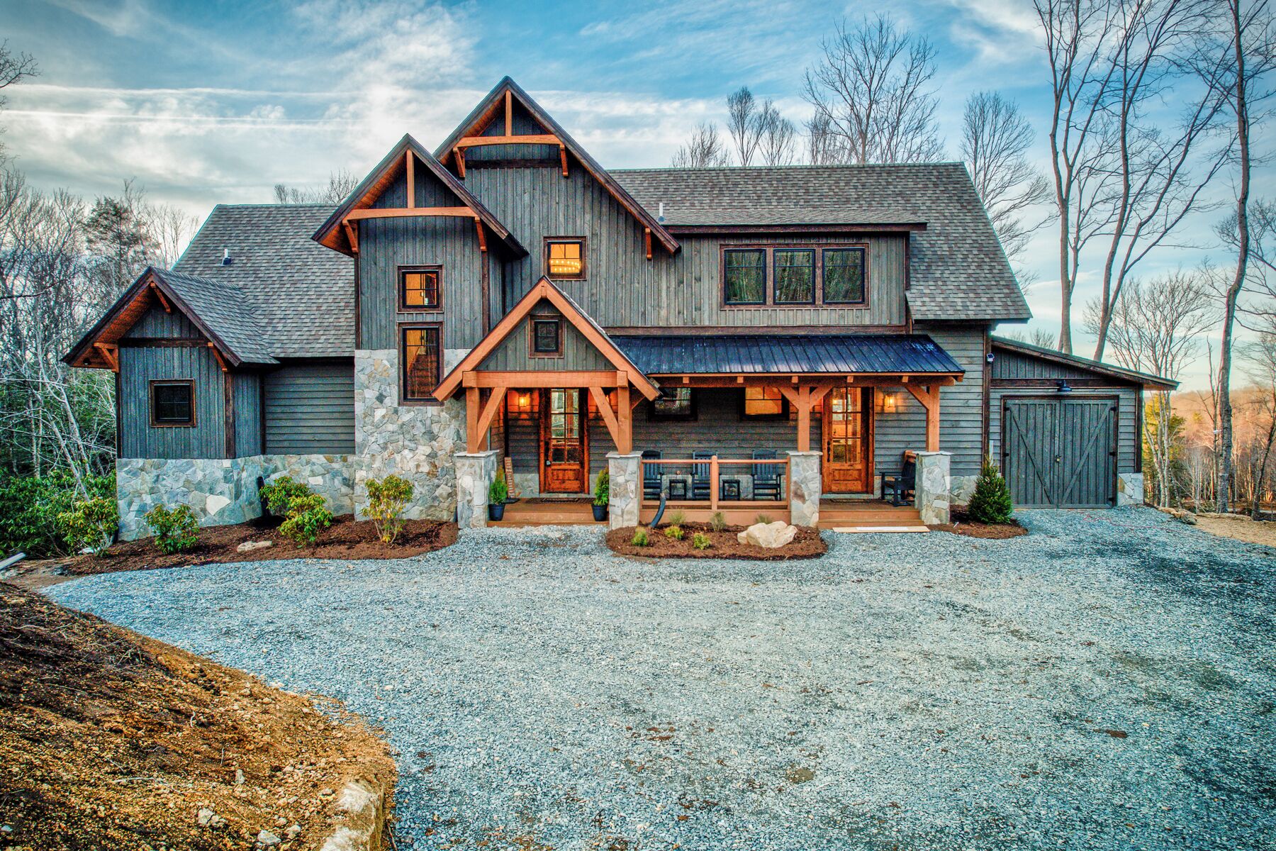 A large, multi-story log cabin with a stone foundation, a covered porch, and a gravel driveway.