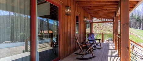 A wooden deck with rocking chairs, a glass door entrance, and a doormat.