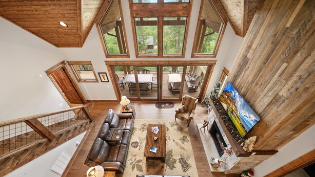 A spacious living area with a high ceiling, wooden beams, and large windows offering a view of the outdoors. - Song on the Mountain at Eagles Nest (Banner Elk)