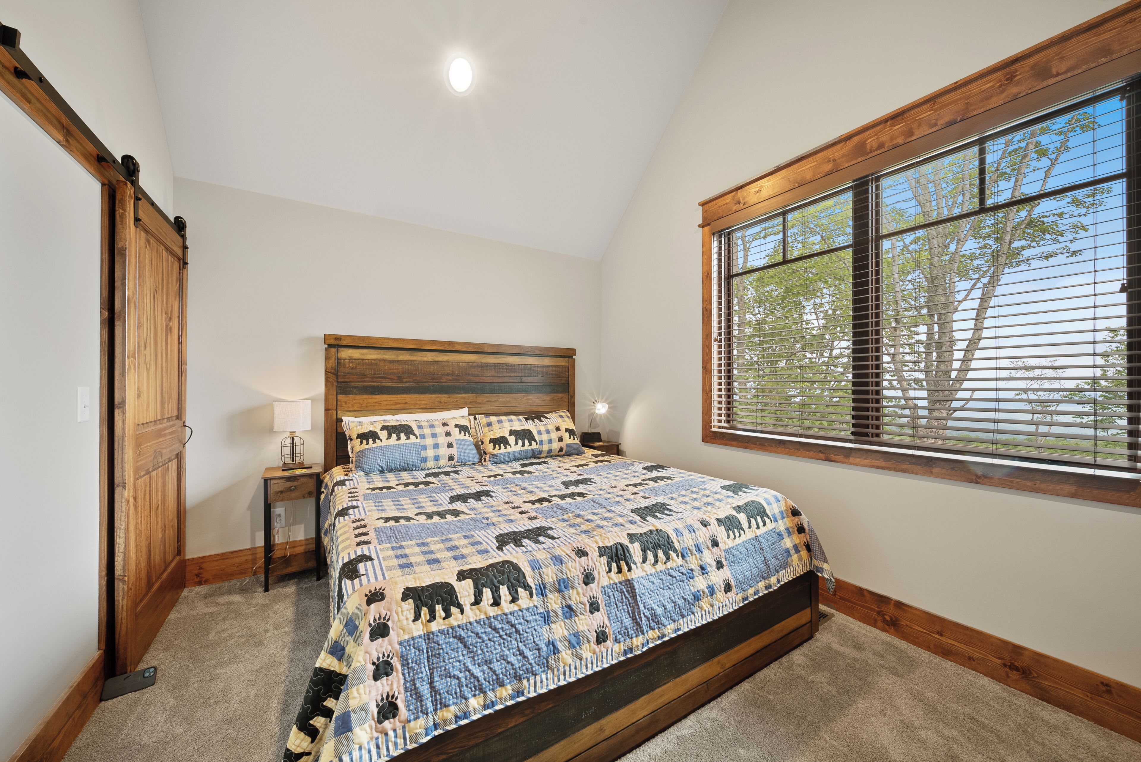 Ein Schlafzimmer mit einem großen Bett, einem Holz-Kopfteil, einem Nachttisch, einer Lampe und einem Fenster mit Jalousien.