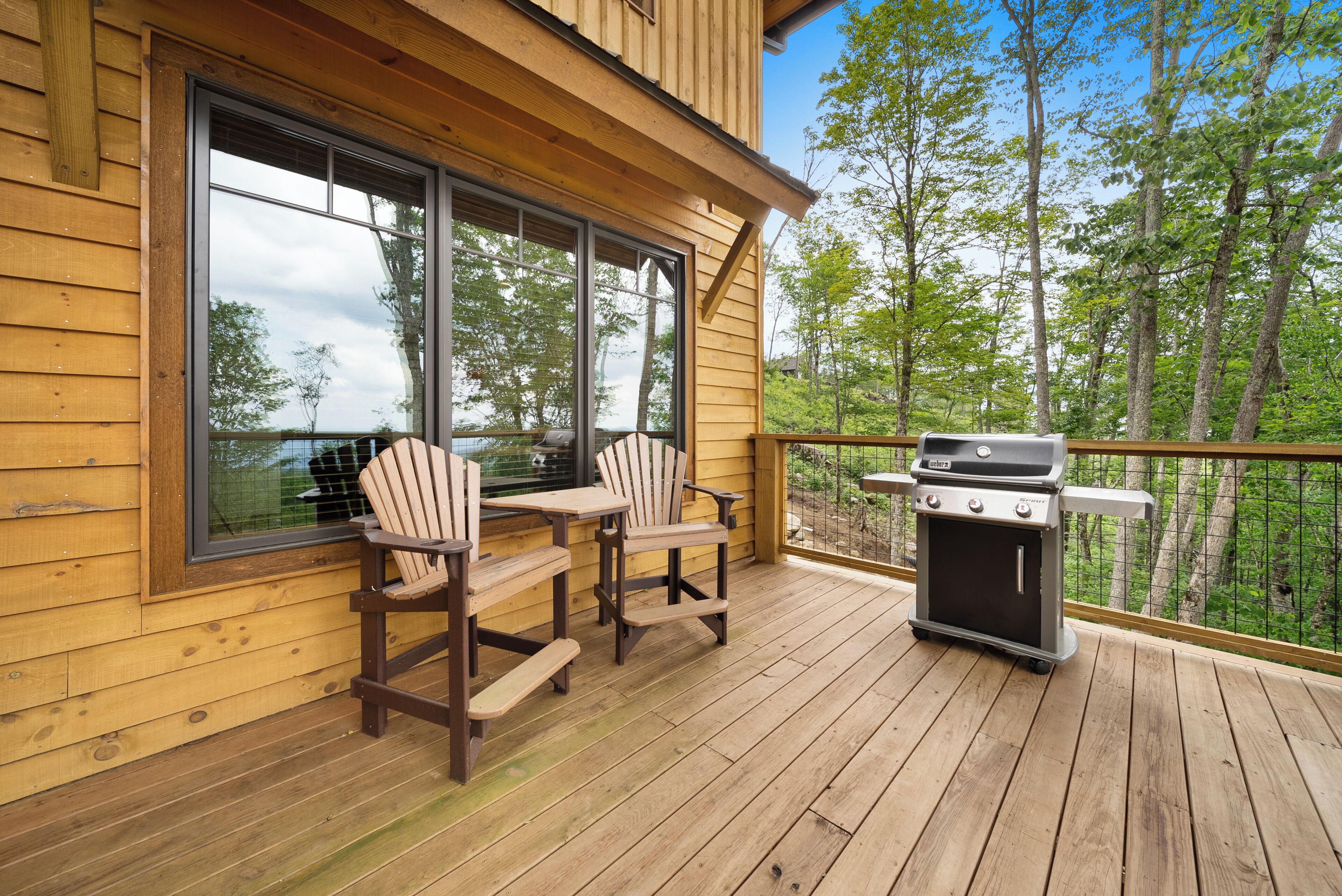 Eine Holzterrasse mit zwei Adirondack-Stühlen und einem Grill.