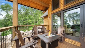 A wooden deck with Adirondack chairs, a fire pit, and a glass door leading to a dining area. - Song on the Mountain at Eagles Nest (Banner Elk)