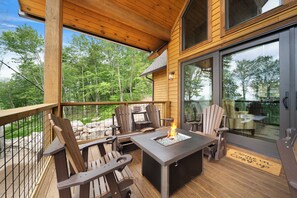 Eine Holzterrasse mit Adirondack-Stühlen, einer Feuerstelle und einer Glastür, die zu einem Essbereich führt.