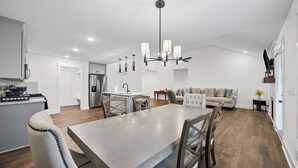 A modern kitchen with a dining area, wooden flooring, and a chandelier.