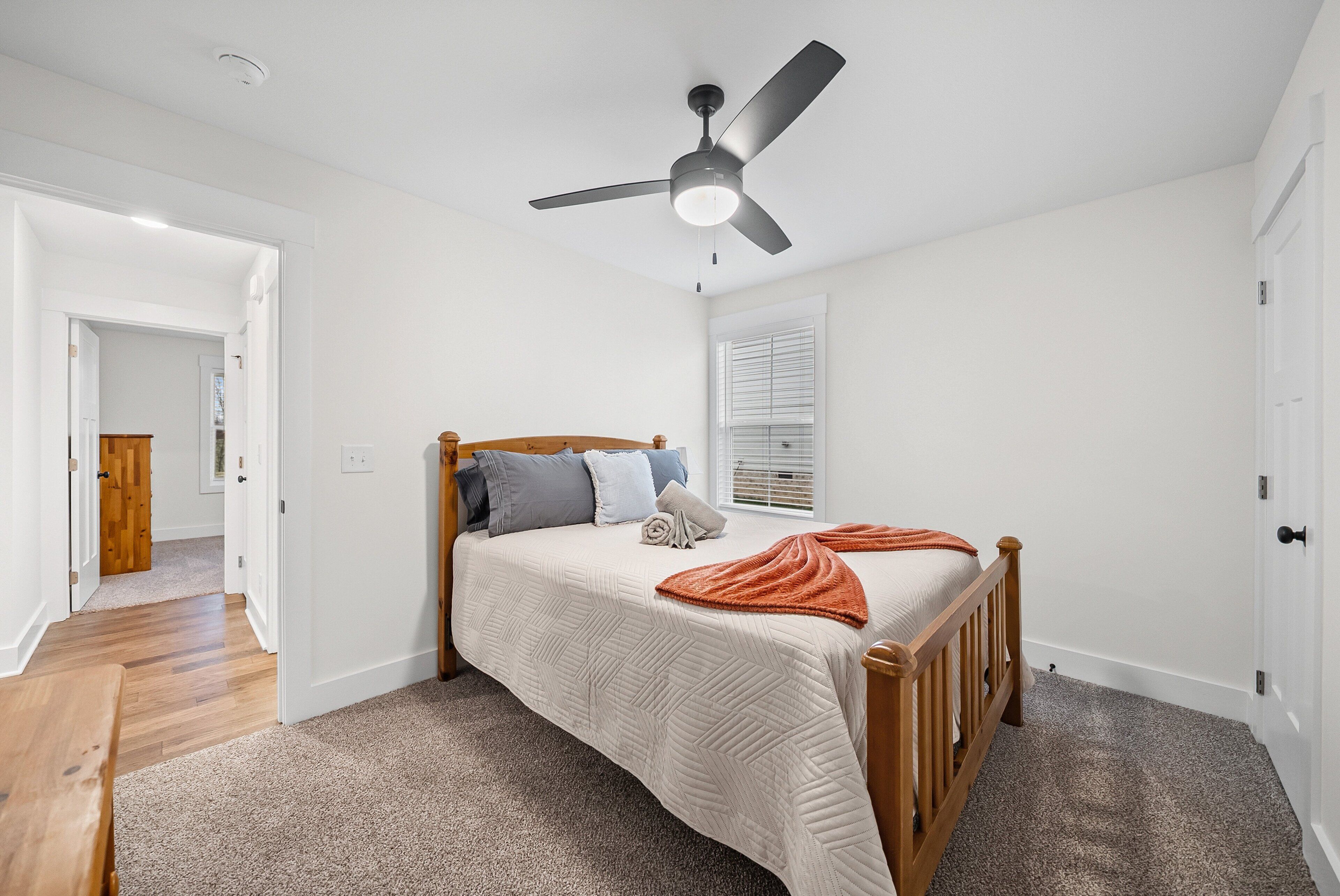 A bedroom with a bed, a ceiling fan, a window with blinds, and a door.