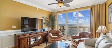 A living room with a TV, leather sofas, a wooden cabinet, and a balcony with a view.