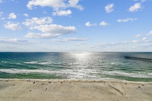 Ein Strand mit einem Steg, der sich ins Meer erstreckt, strahlend blauer Himmel und ruhige Wellen.