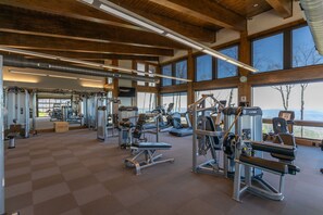 A gym with various exercise machines, large windows, and a high ceiling with exposed beams.