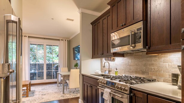 A modern kitchen with dark wooden cabinets, stainless steel appliances, and a stone backsplash.