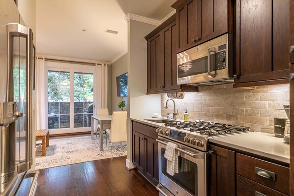 A modern kitchen with dark wooden cabinets, stainless steel appliances, and a stone backsplash. - Cozy Mountain Retreat at Blue Ridge Mountain Club (Boone)