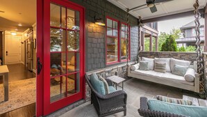 A covered porch with a swing seat, wicker furniture, and a red-framed window.