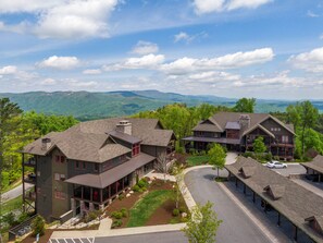 A large, multi-story hotel with a central courtyard, surrounded by lush greenery and mountains in the background. - Cozy Mountain Retreat at Blue Ridge Mountain Club (Boone)