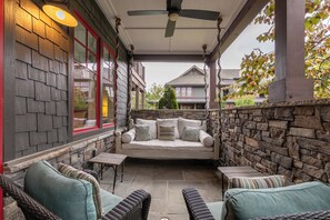 A covered patio with a stone wall, a white sofa, wicker chairs, and a ceiling fan.