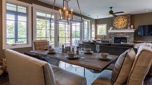 A spacious living room with a large dining table set for six, a fireplace, and a stone accent wall.