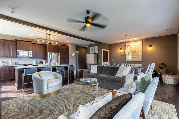 A modern living room with a sofa, coffee table, and a dining area with a kitchen in the background.