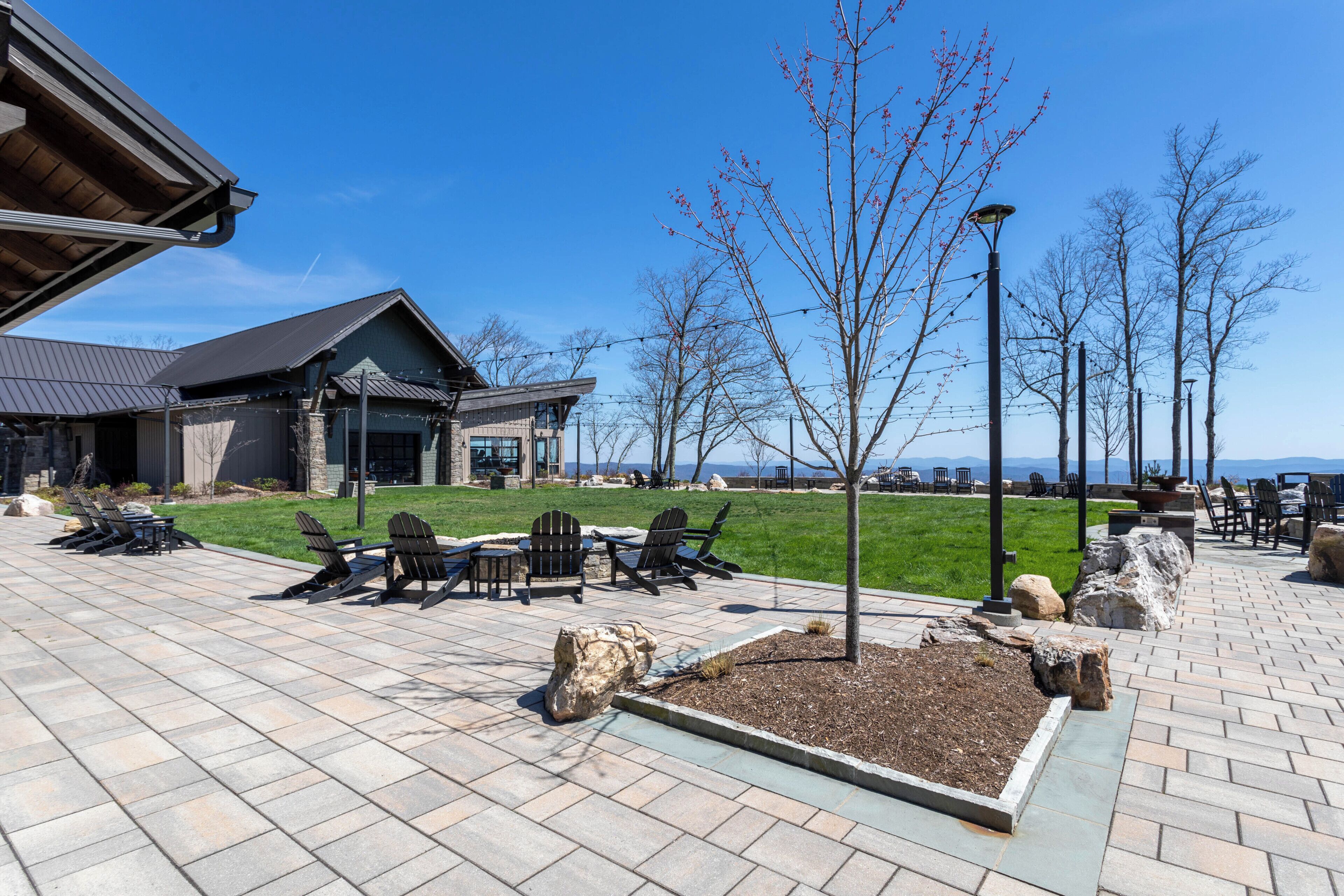 A patio area with Adirondack chairs, a fire pit, and a view of a building with a sloped roof.