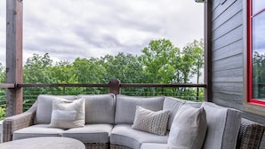 A covered outdoor seating area with a curved wicker sofa and a round table.