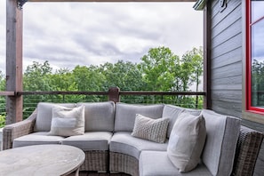 A covered outdoor seating area with a curved wicker sofa and a round table.