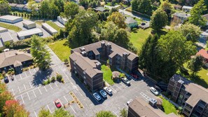 An aerial view of a residential complex with multiple apartment buildings, a parking lot, and surrounding greenery.
