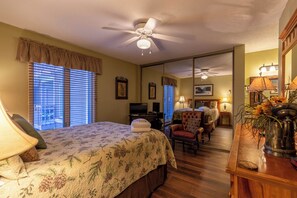 Quarto de hotel com cama, escrivaninha, cadeira, televisão e ventoinha no teto.