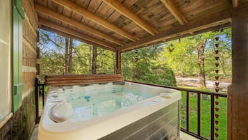 A hot tub under a wooden pergola with a view of a landscaped garden.