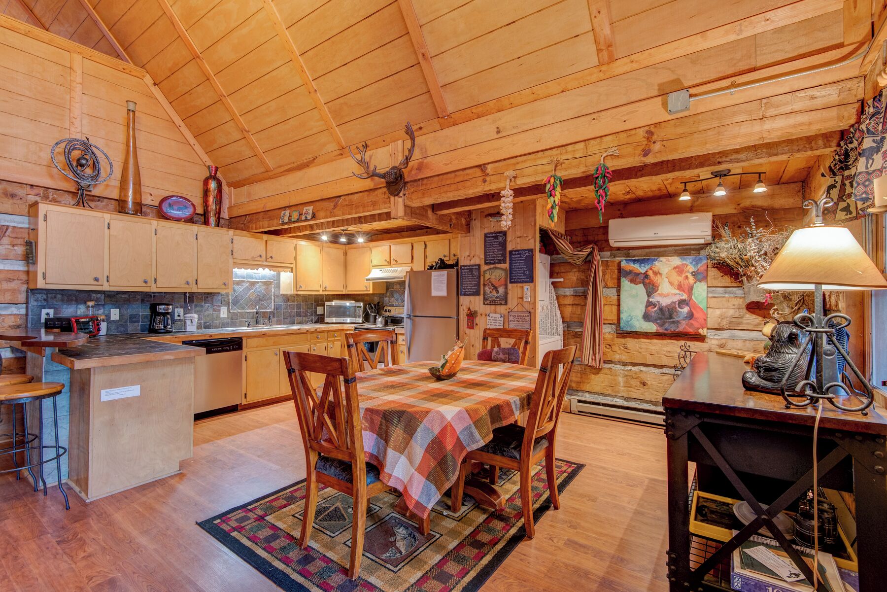 A rustic cabin-style kitchen with wooden cabinets, a dining table with chairs, and a hanging light fixture.
