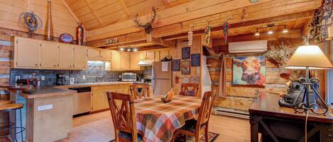 A rustic cabin-style kitchen with wooden cabinets, a dining table with chairs, and a hanging light fixture.