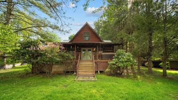 A cabin with a front porch, a wooden deck, and a grassy yard.