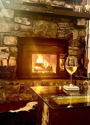 Ein Kamin aus Stein mit Feuer, ein Weinglas auf einem Untersetzer und eine Steinsäule.