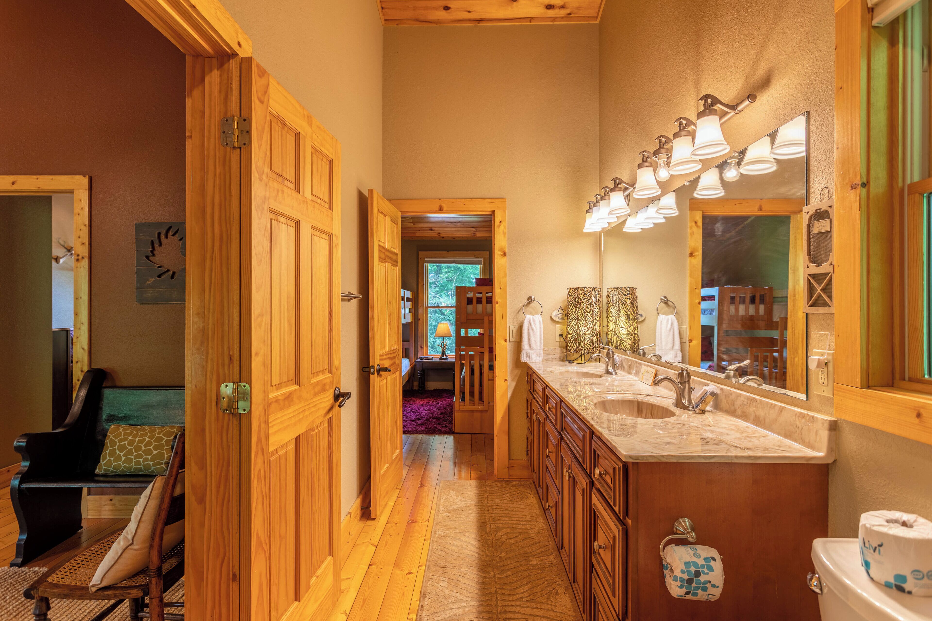 A wooden hallway leading to a bathroom with a large sink, mirror, and toilet.