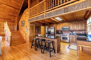 A wooden interior with a kitchen, bar stools, and a staircase. - Azalea Hill - Mountain Views, Hot Tub, Pool Table, Ping Pong (Boone)