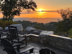 Ein Sitzbereich im Freien mit Steinmauern und Blick auf einen Sonnenuntergang über einer Berglandschaft.