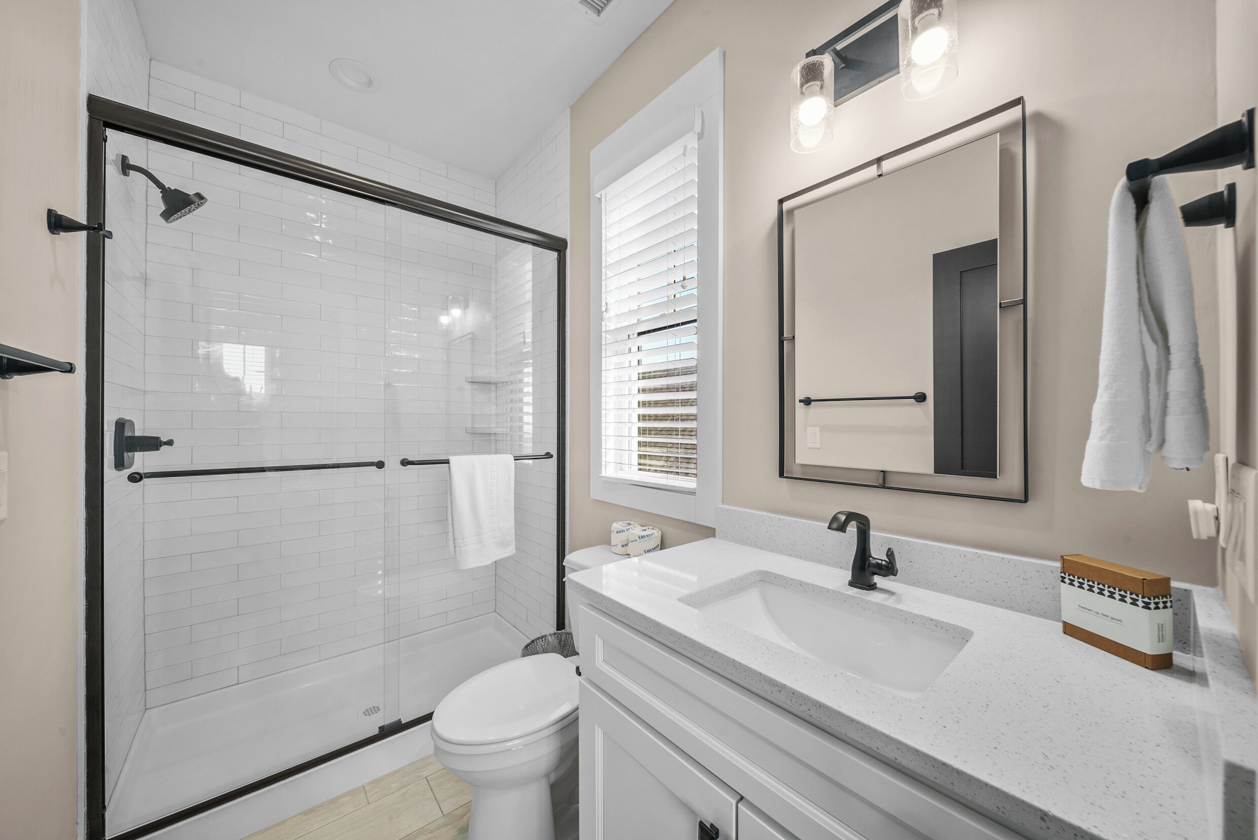 A modern bathroom with a glass-enclosed shower, a white toilet, a large mirror, and a countertop with a sink.
