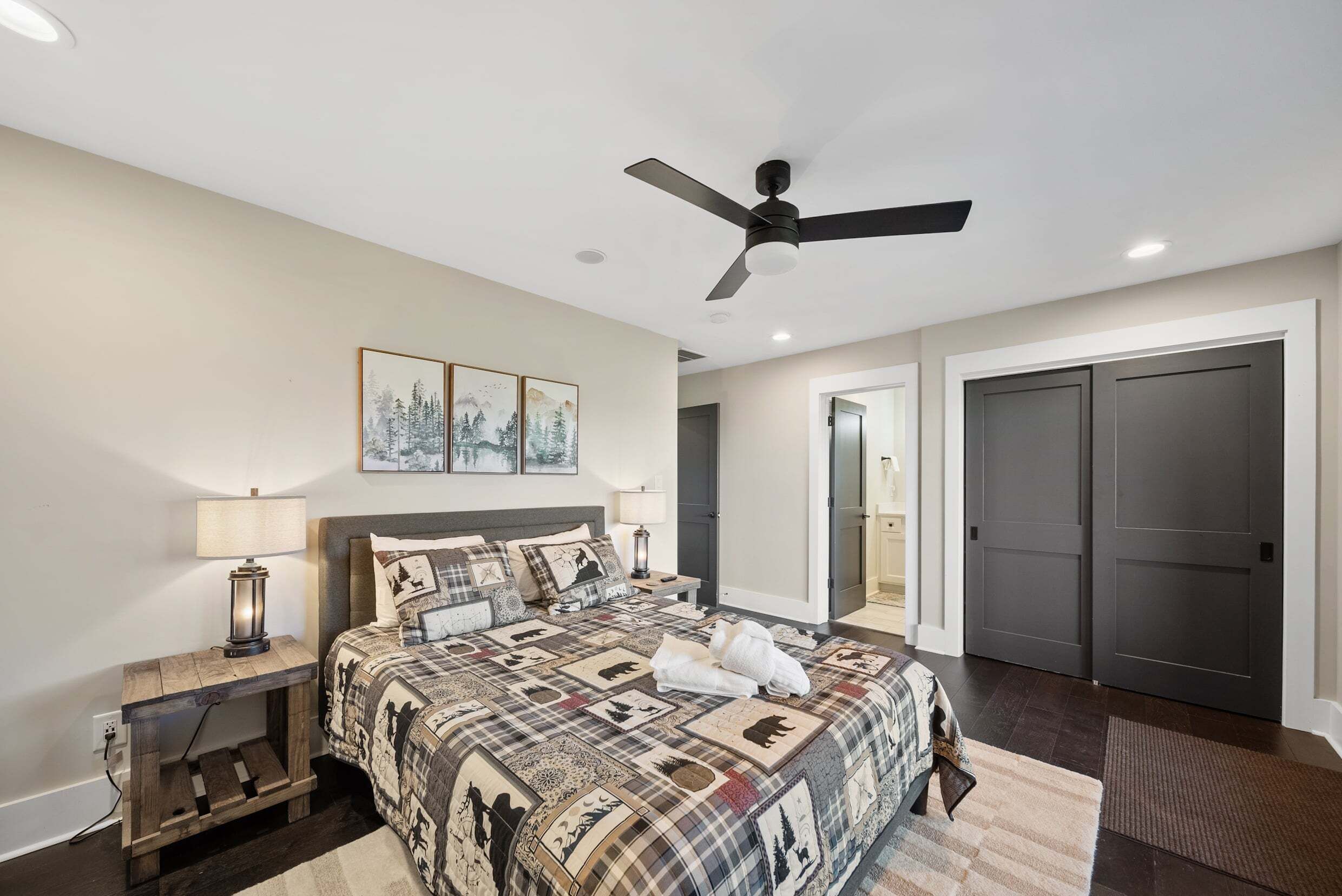 A bedroom with a bed, a ceiling fan, a nightstand, a lamp, and a door.