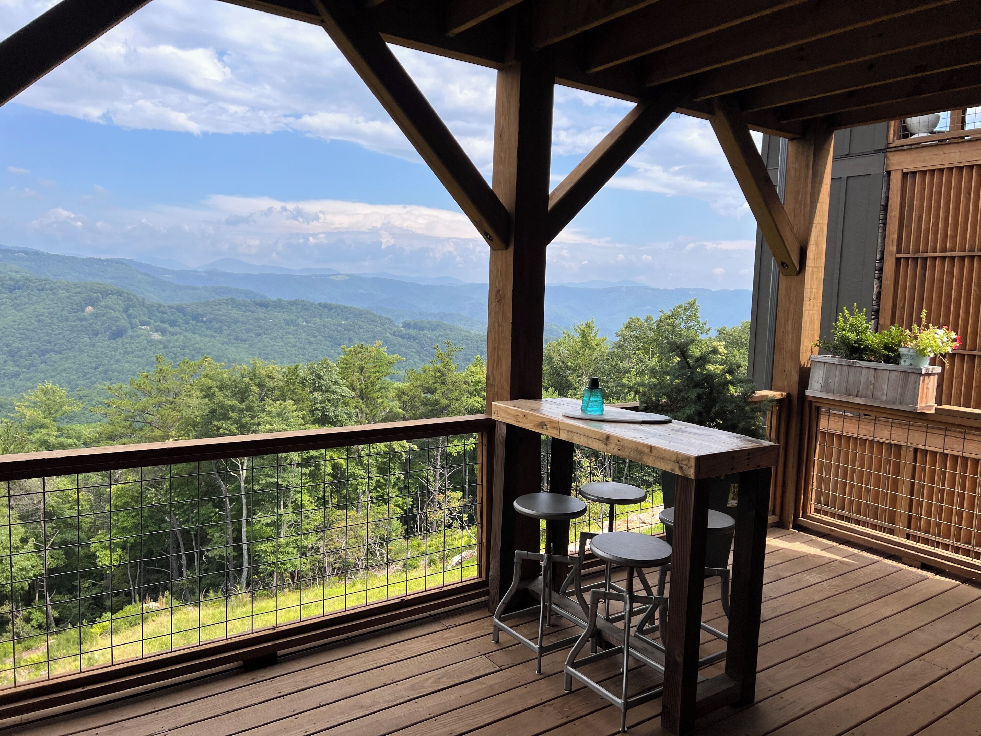 A wooden deck with a table and stools, overlooking a mountainous landscape.