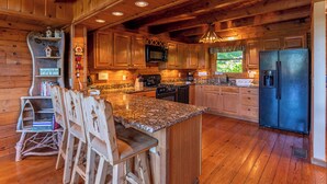 A cabin-style kitchen with wooden cabinets, granite countertops, a built-in stove, and a refrigerator. - Apple of my Eye (Banner Elk)